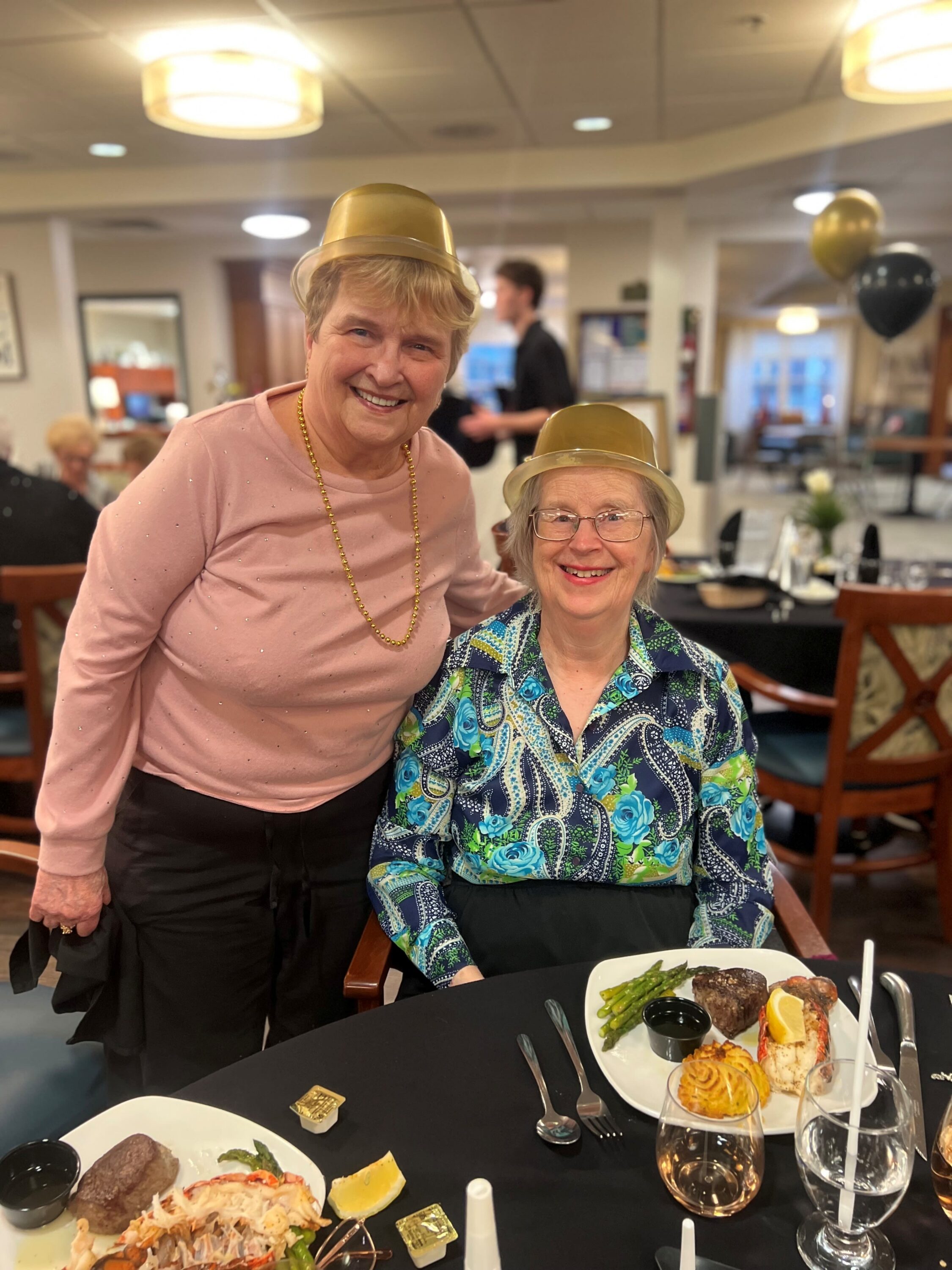 Two elderly women in gold hats at dinner