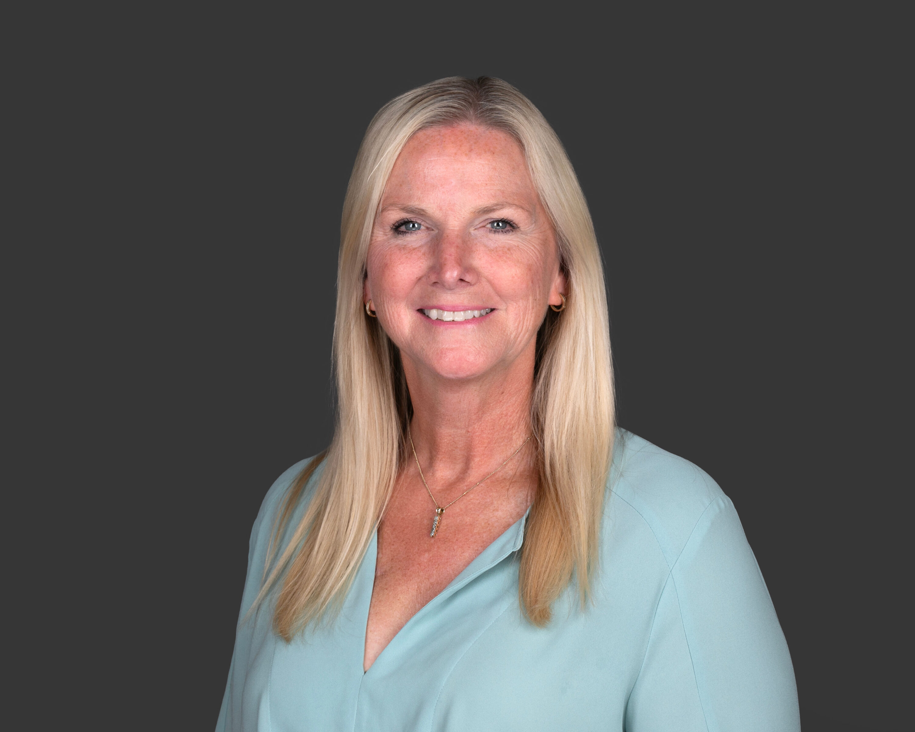 Professional headshot of smiling blonde woman on gray background