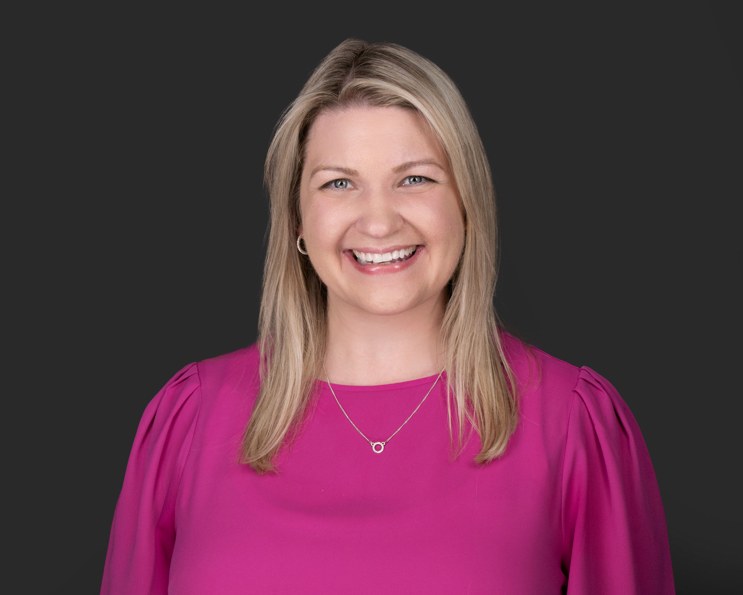Smiling woman in pink blouse against dark background
